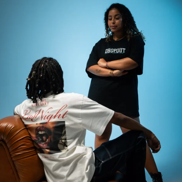 Flacko sits wearing the Hangover Oversized Black T-shirt while looking at Júlia who is wearing the Teddy Bear Streetwear T-shirt from the Dropout brand.