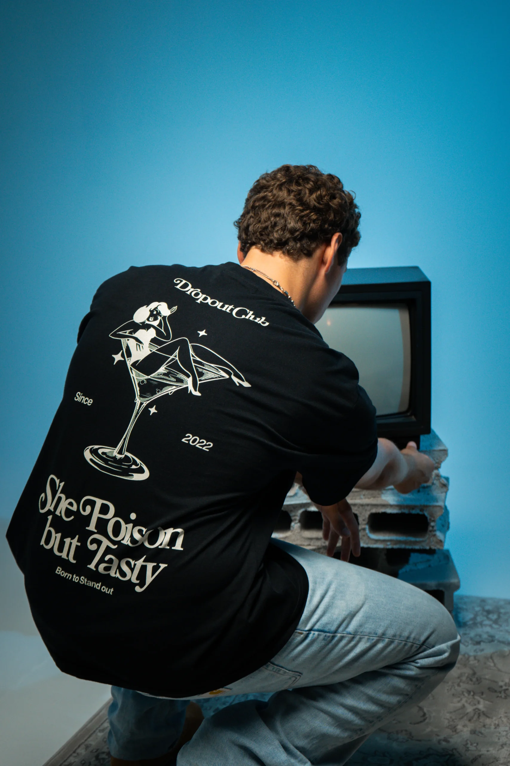 Gustavo wearing a Tasty Poison Black T-shirt by Dropout, turning up the volume on the television